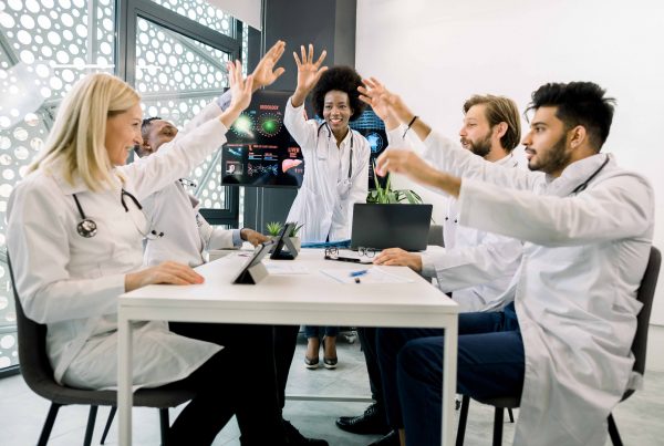 Grupo de doutores ou cientistas motivados, sentado ao redor da mesa na sala de conferências da clínica moderna, dando um gesto de cinco com as mãos, depois de um ótimo trabalho em equipe.